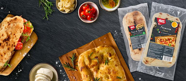 Schwarzer Hintergrund mit einem zubereiteten Foccacia und Pane di Napoli. Rechts beide Produkte in ihrer Verpackung