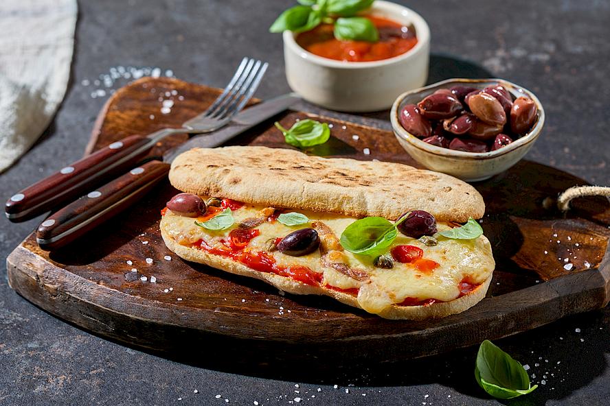 Rezeptidee: Pane di Napoli bestrichen mit Tomatensauce und mit einigen roten Chiliringen belegt. Mit geriebenem Käse bestreut. Darauf einige Sardellen, Kapern und Oliven verteilen. Goldbraun überbacken und mit Basilikum garnieren.
