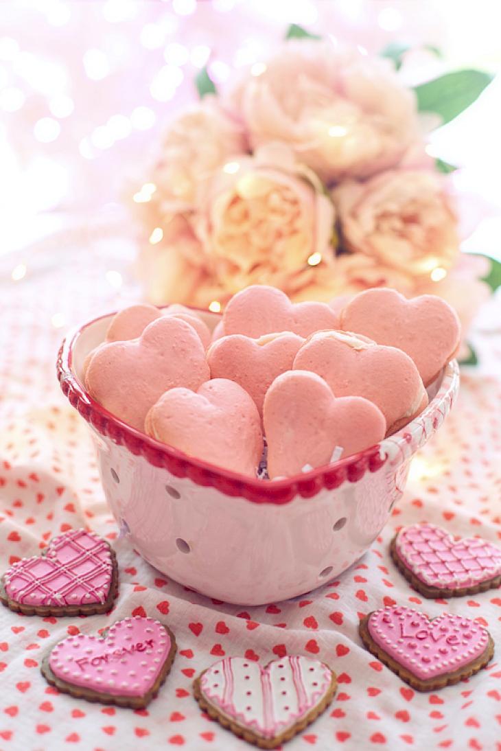 Heart-shaped bowl with pink heart cookies on a tablecloth with red hearts; additional decorated cookies with the words “Forever” and “Love” in the foreground.